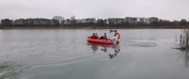 Trzech strażaków w łodzi ratowniczej ocenia rozmiar plamy na tafli jeziora.