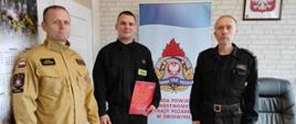 na zdjęciu po lewej ubrany w piaskowy strój koszarowy dowódca jednostki,na środku strażak ze świadectwem ukończenia kursu w dłoni, po prawej komendant jednostki ubrany na czarno 