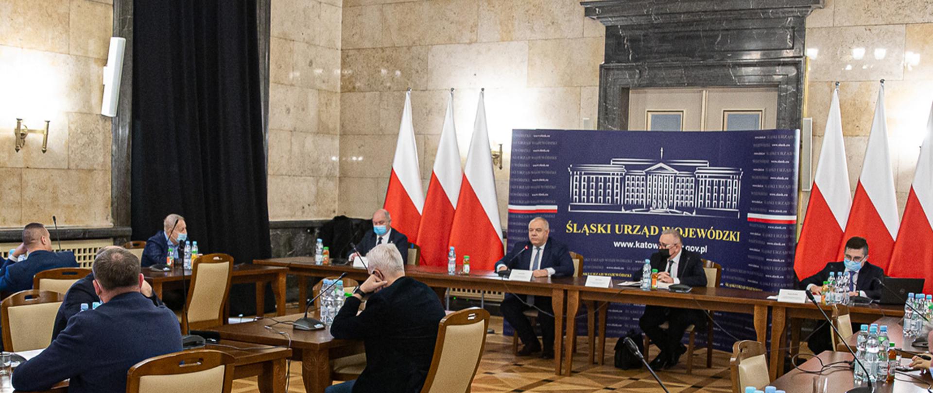 Na pierwszym planie siedzą związkowcy, dalej wicepremier Jacek Sasin i wiceminister Piotr Pyzik. W tle ścianka z napisem Śląski Urząd Wojewódzki oraz flagi. 