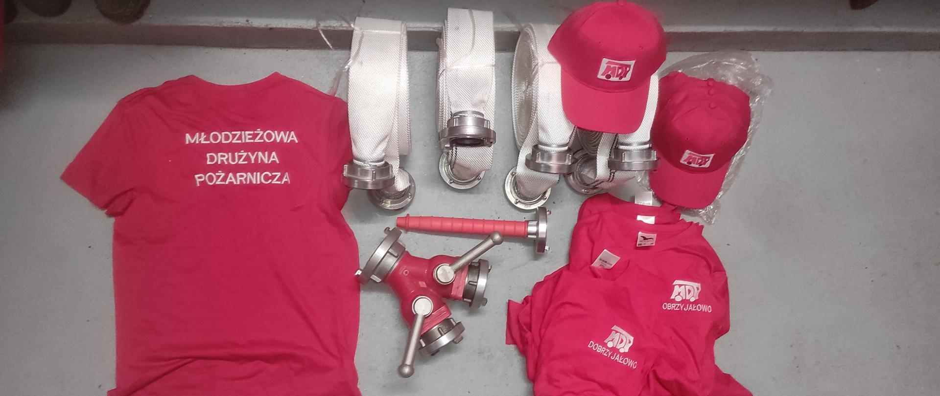 Na ziemi leżą koszulki, obok znajdują się węże pożarnicze, prądownica oraz rozdzielacz.