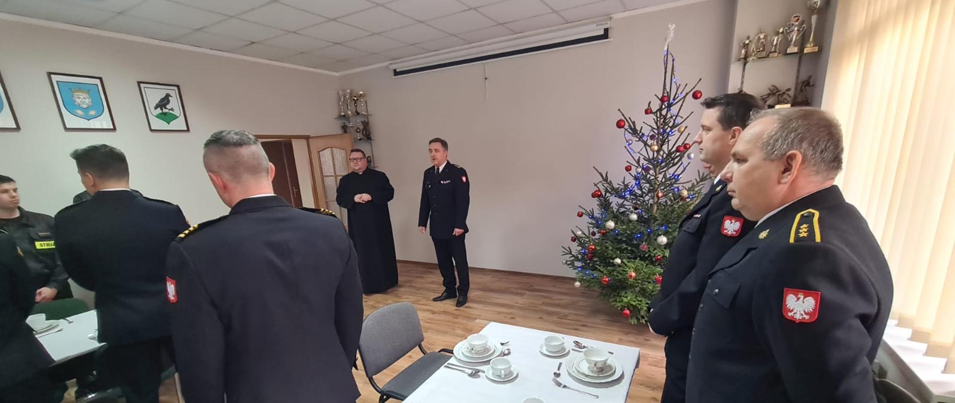 Po lewej strażacy, na środku kapelan strażaków i komendant powiatowy, po prawej choinka i dwóch strażaków