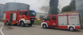 Zdjęcie przedstawia samochody pożarnicze na tle zbiorników przeciwpożarowych i budynków zakładu