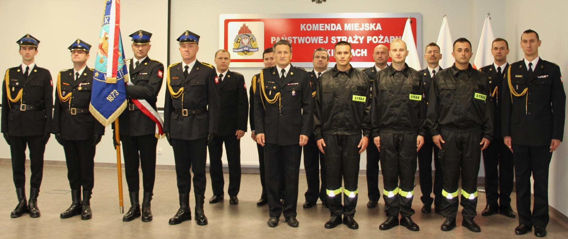 Zdjęcie przedstawia wszystkich uczestników ślubowania. W pierwszym szeregu stoją nowi strażacy wraz z komendantem miejskim i jego zastępcą, z lewej strony stoi poczet sztandarowy ze sztandarem, a w drugim rzędzie pracownicy Komendy Miejskiej Państwowej Straży Pożarnej w Kielcach.