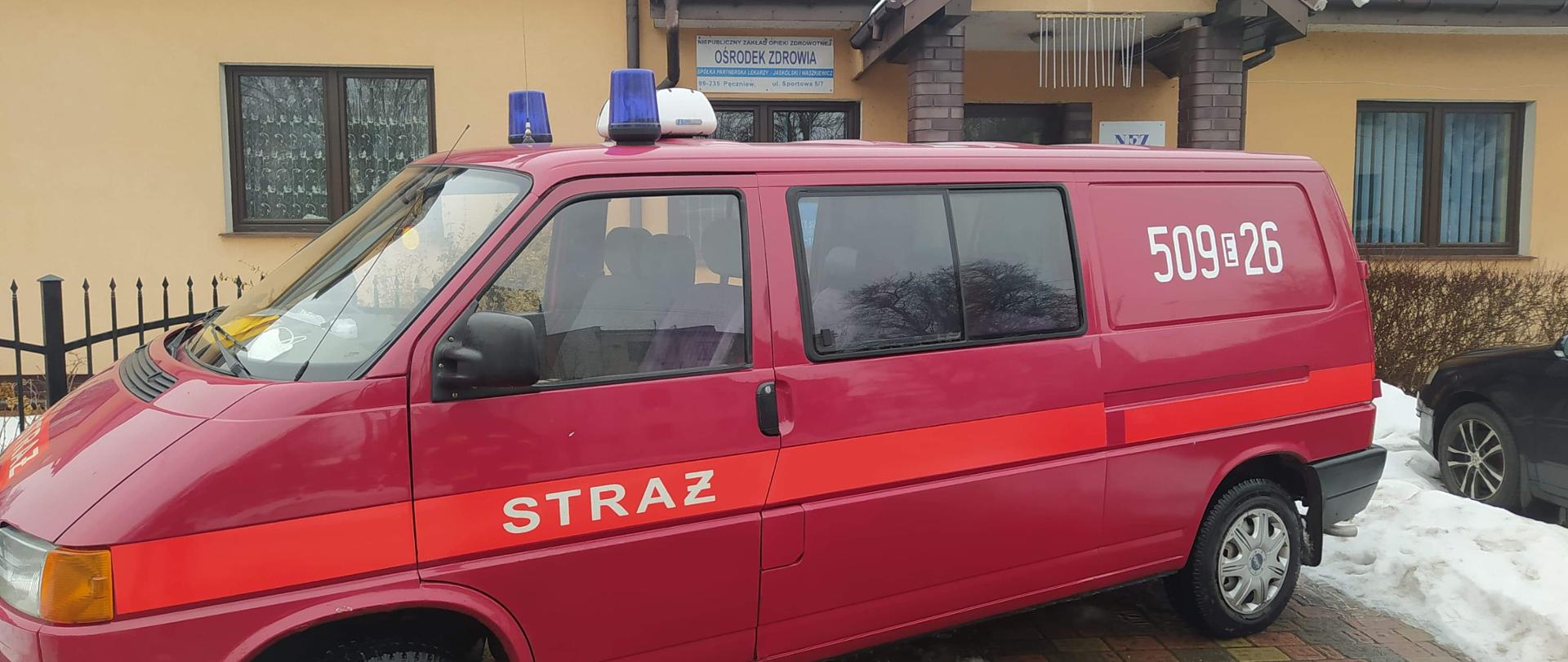 Samochód strażacki czerwony z białym napisem straż i numerem 509E26 na tle budynku ośrodku zdrowia