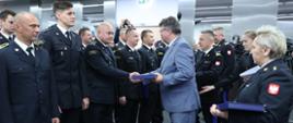 Na zdjęciu widać Wiceministra MSWiA Macieja Wąsika w trakcie wręczania nagród i wyróżnień. Obok stoi komendant główny PSP gen. brygadier Andrzej Bartkowiak a także jego zastępcy którzy podają rękę wyróżnionym strażakom.