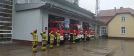 Strażacy przed budynkiem JRG, w tle pojazdy.