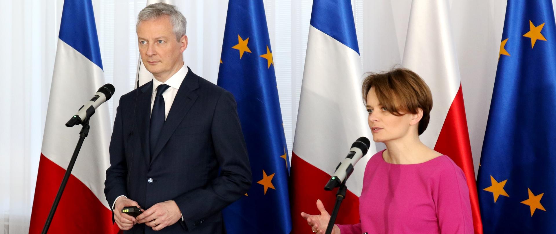 Ministrowie Bruno Le Maire i Jadwiga Emilewicz stoją na tle flag Francji, Polski i Unii Europejskiej