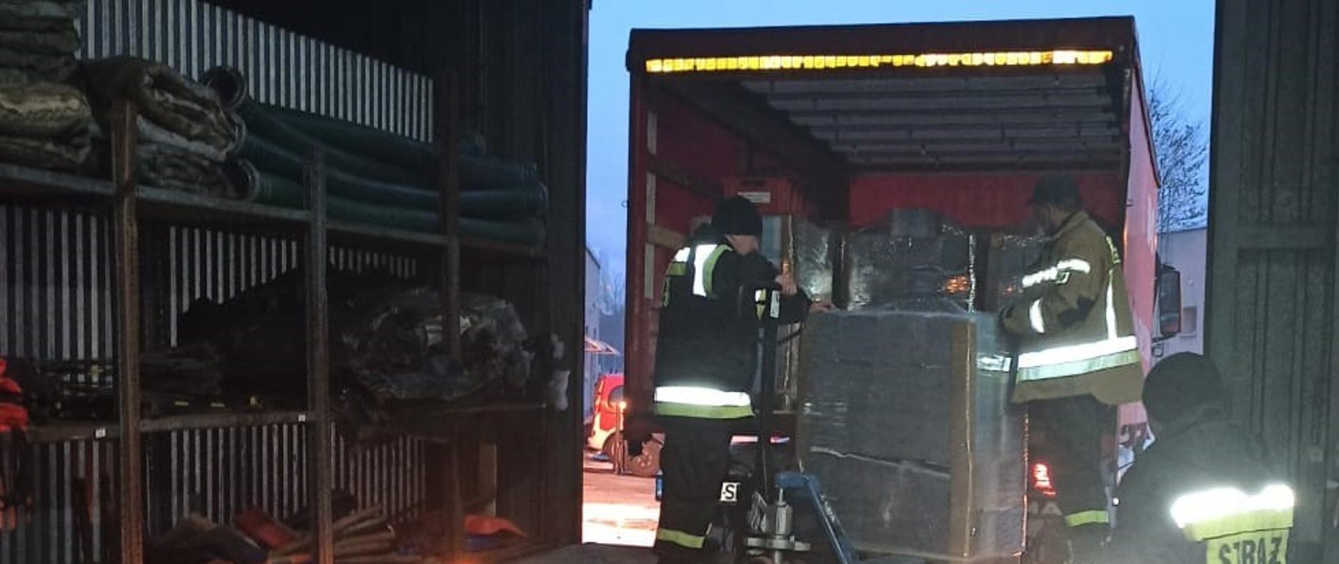 Rozładunek pojazdu pożarniczego z ulotkami promującymi akcję szczepień.