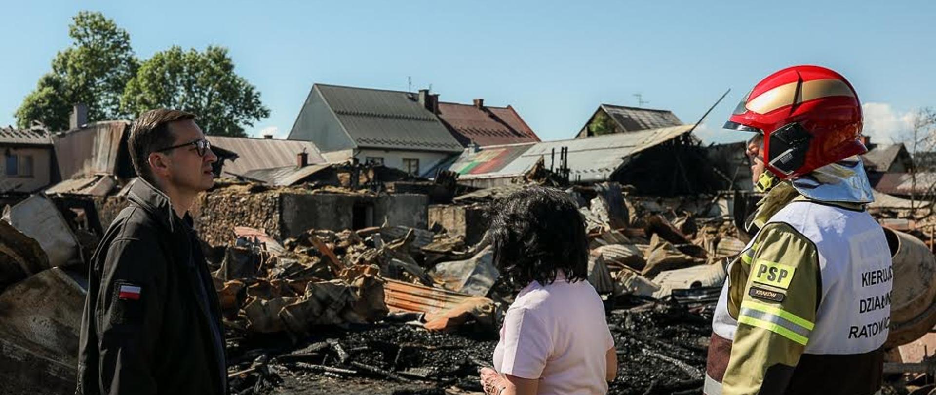 Premier Mateusz Morawiecki patrzy się na zniszczone przez pożar budynki.