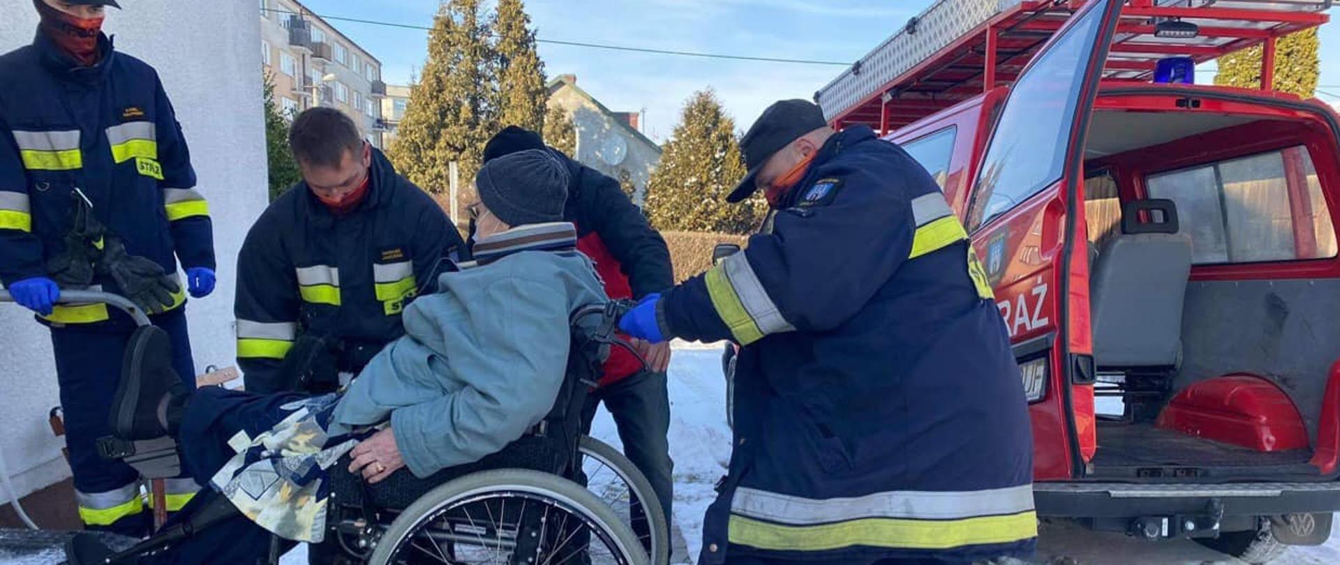 Na zdjęciu znajduje się osoba będąca na wózku inwalidzkim którą strażacy dostarczyli do punktu szczepień na pandemię COVID-19.