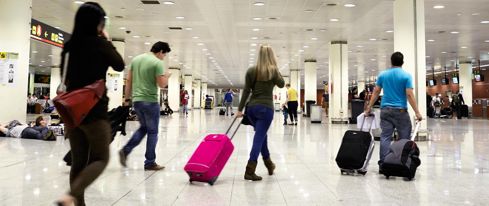 Ludzie z walizkami idą przez halę na lotnisku.