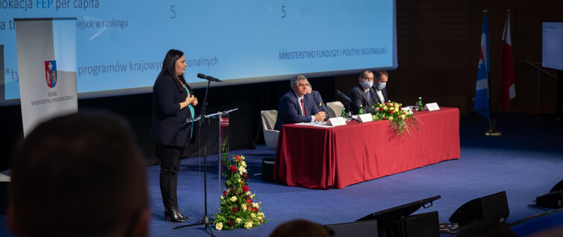 Minister Jarosińska-Jedynak stoi na scenie i mówi do mikrofonu 