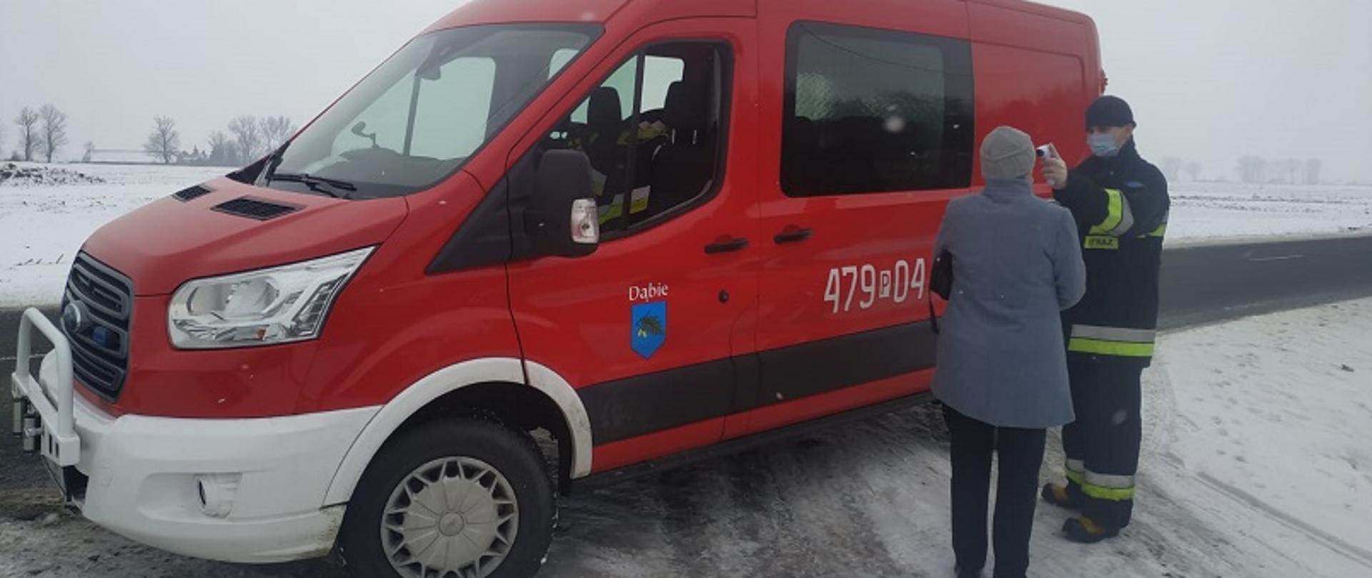 Zdjęcie przedstawia strażaka jednostki OSP, który mierzy temperaturę osobie starszej przewożonej do punktu szczepień.