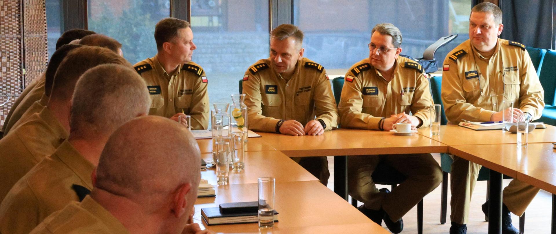 Narada szkoleniowa pionów logistycznego i finansowego Państwowej Straży Pożarnej województwa podlaskiego - spotkanie kadry kierowniczej na czele z komendantem wojewódzkim PSP. Wszyscy siedzą przy stołach, w tle okna sali