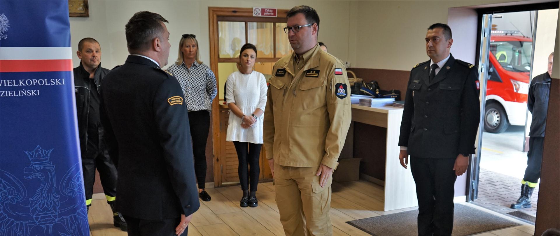 składanie meldunku przez strażaka drugiemu strażakowi, w tle grupa osób