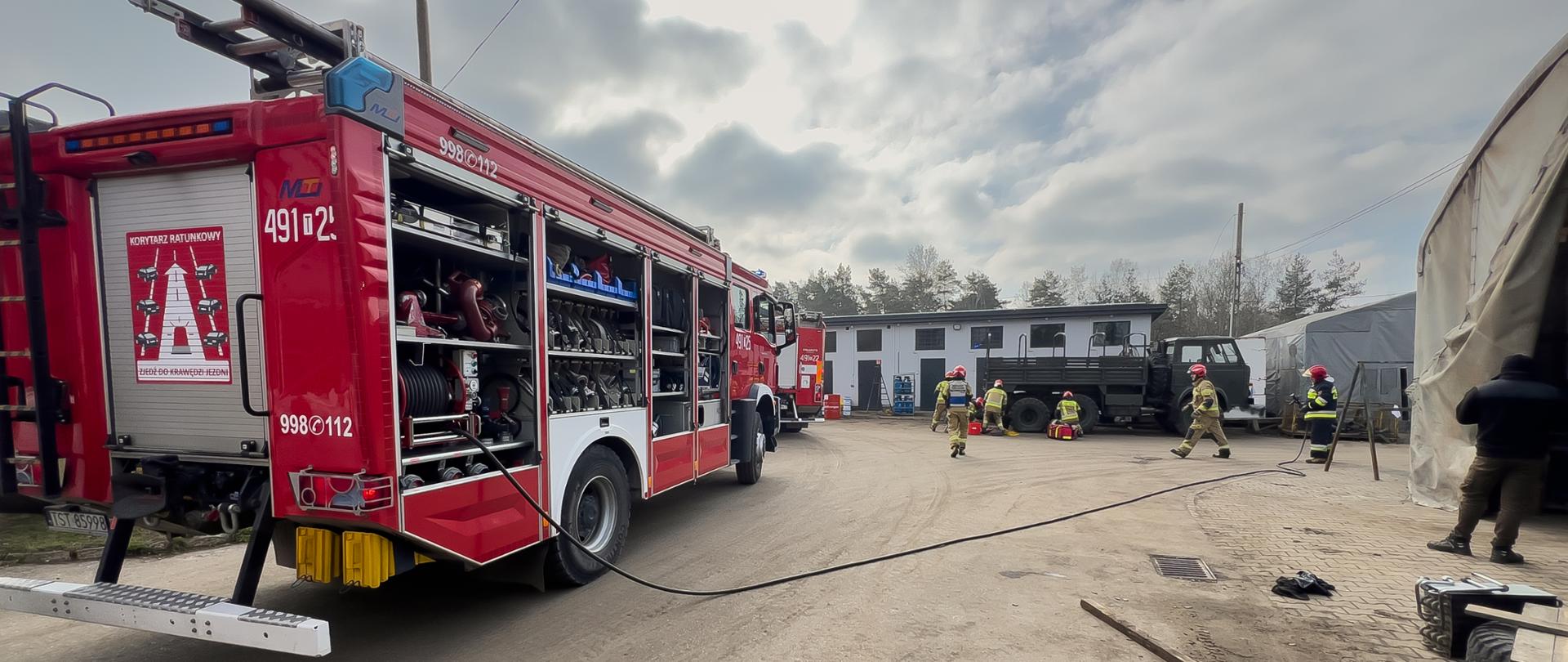 Na pierwszym planie wóz bojowy, w tle widoczni strażacy biorący udział w ćwiczeniach
