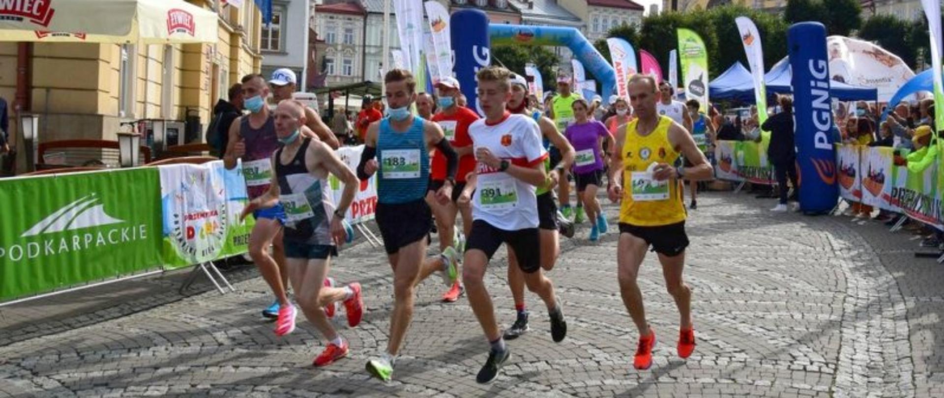 Zmagania strażaków w biegu „Przemyska Dycha” – na zdjęciu zmagania zawodników na trasie – zwarta grupa kolorowo ubranych sportowców – po obu stronach trasy kibice