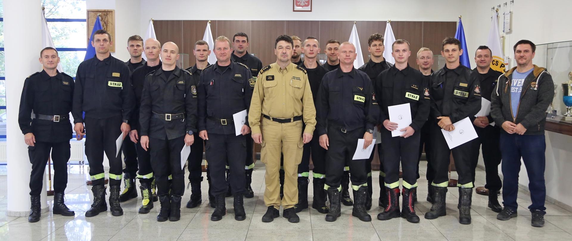 Grupowe zdjęcie uczestników szkolenia (15 osób) w towarzystwie Komendanta Centralnej Szkoły PSP wraz z dwójką funkcjonariuszy CS PSP oraz wykładowcy