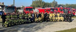 Grupa strażaków biorąca udział w manewrach na tle pojazdów pożarniczych