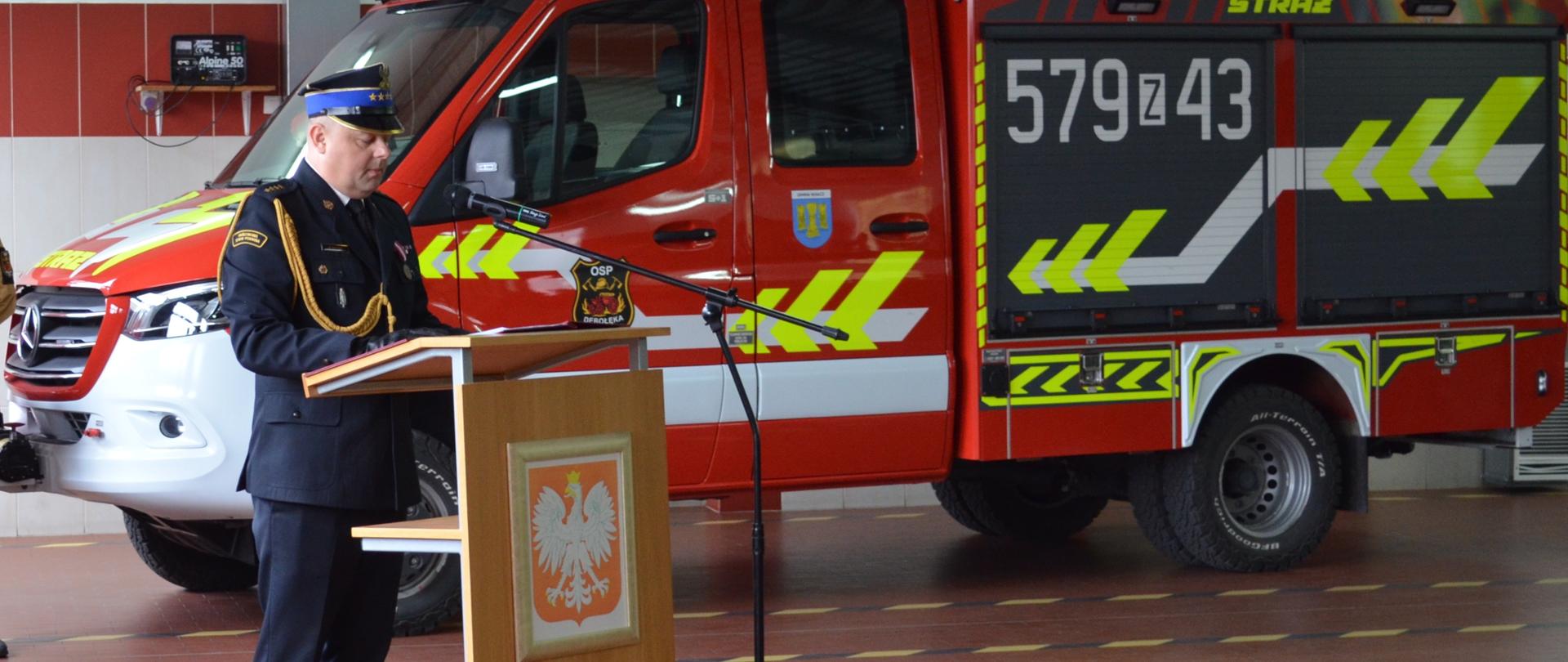 Na zdjęciu znajduje się Komendant Powiatowy PSP w Wałczu w trakcie oficjalnego wystąpienia z okazji obchodów Dnia Strażaka. W tle nowy samochód OSP Dębołeka. 