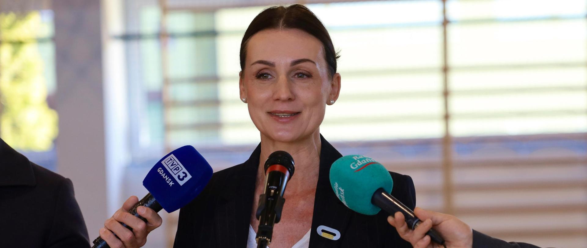 kobieta przemawia stojąc w hali sportowej, obok dziennikarze z mikrofonami, Lębork 21. 04.2026