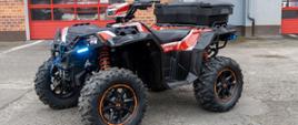 Nowy quad Polaris z terenowym zawieszeniem i skrzynią transportową zaparkowany przed strażnicą, ukazujący pojazd przeznaczony do szybkiego dotarcia do poszkodowanych w trudno dostępnych miejscach.