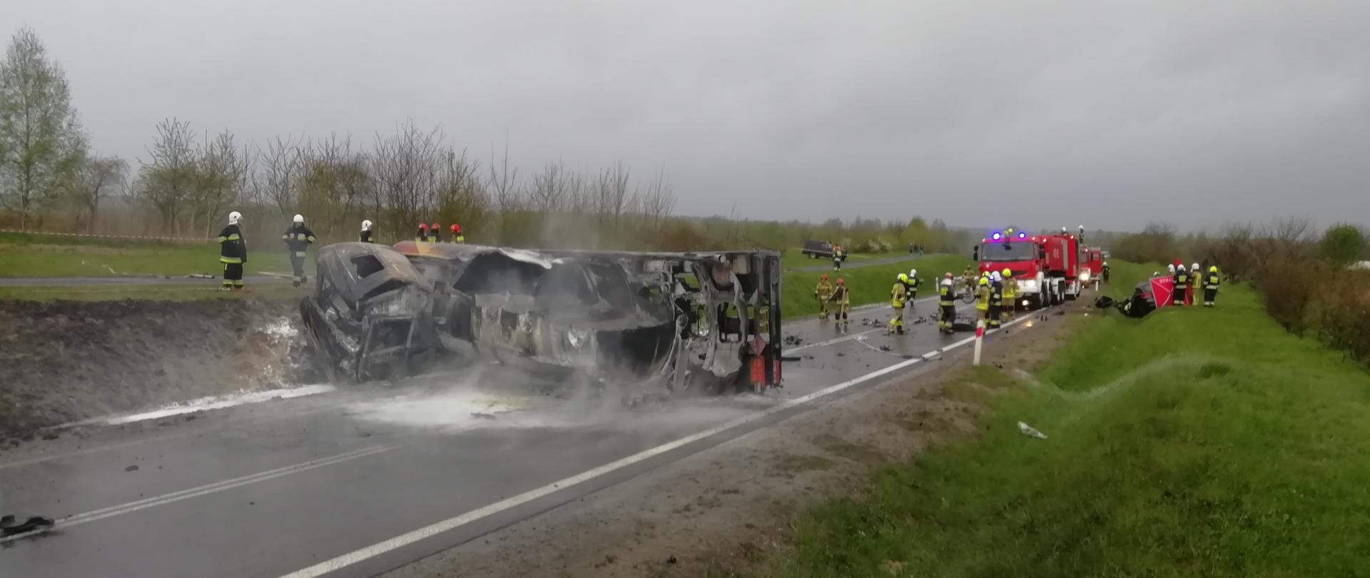 Na zdjęciu widzimy scenę po wypadku cysterny z samochodem osobowym. Cysterna leży w poprzek drogi w koło znajdują się strażacy.