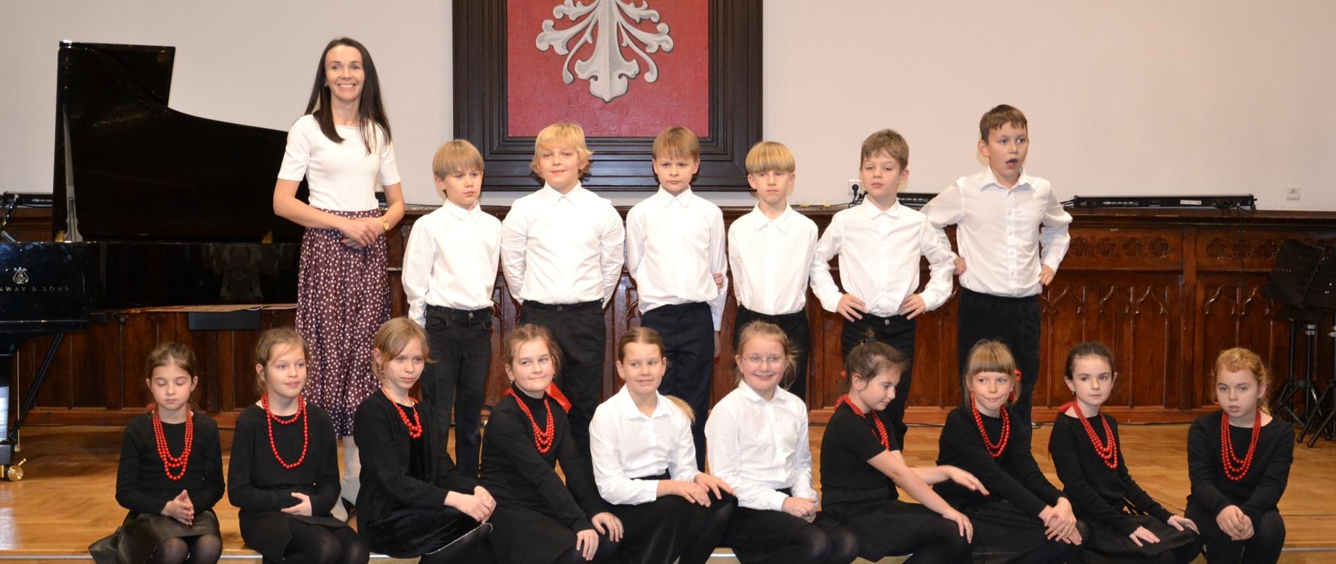 uczniowie w strojach ludowych wraz z nauczycielką na scenie w sali królewskiej psm mielec