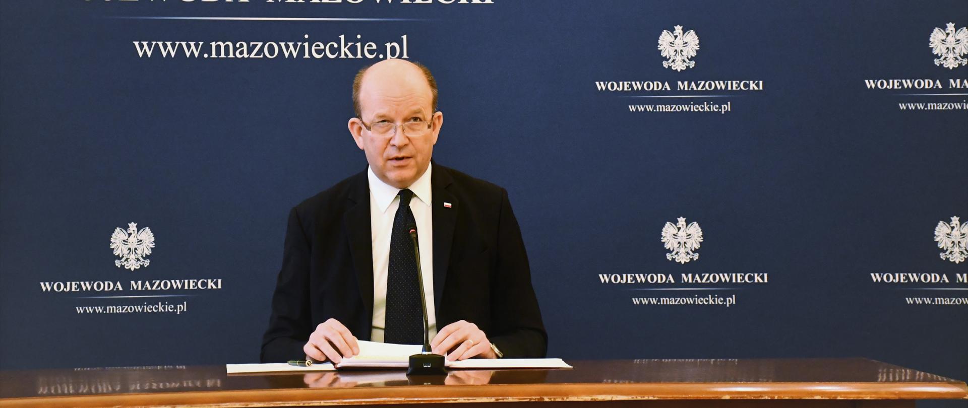 Na zdjęciu Wojewoda Mazowiecki Konstanty Radziwiłł siedzący przy stole. Mówi do mikrofonu. W tle granatowa ścianka z logiem Wojewody przedstawiającym orła białego z napisem Wojewoda Mazowiecki. 