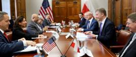 Minister Piotr Nowak z Sekretarz Stanu ds. Handlu, Giną Raimondo, siedzą przy stole wraz z pozostałymi uczestnikami spotkania, na pierwszym planie flagi polska i amerykańska 