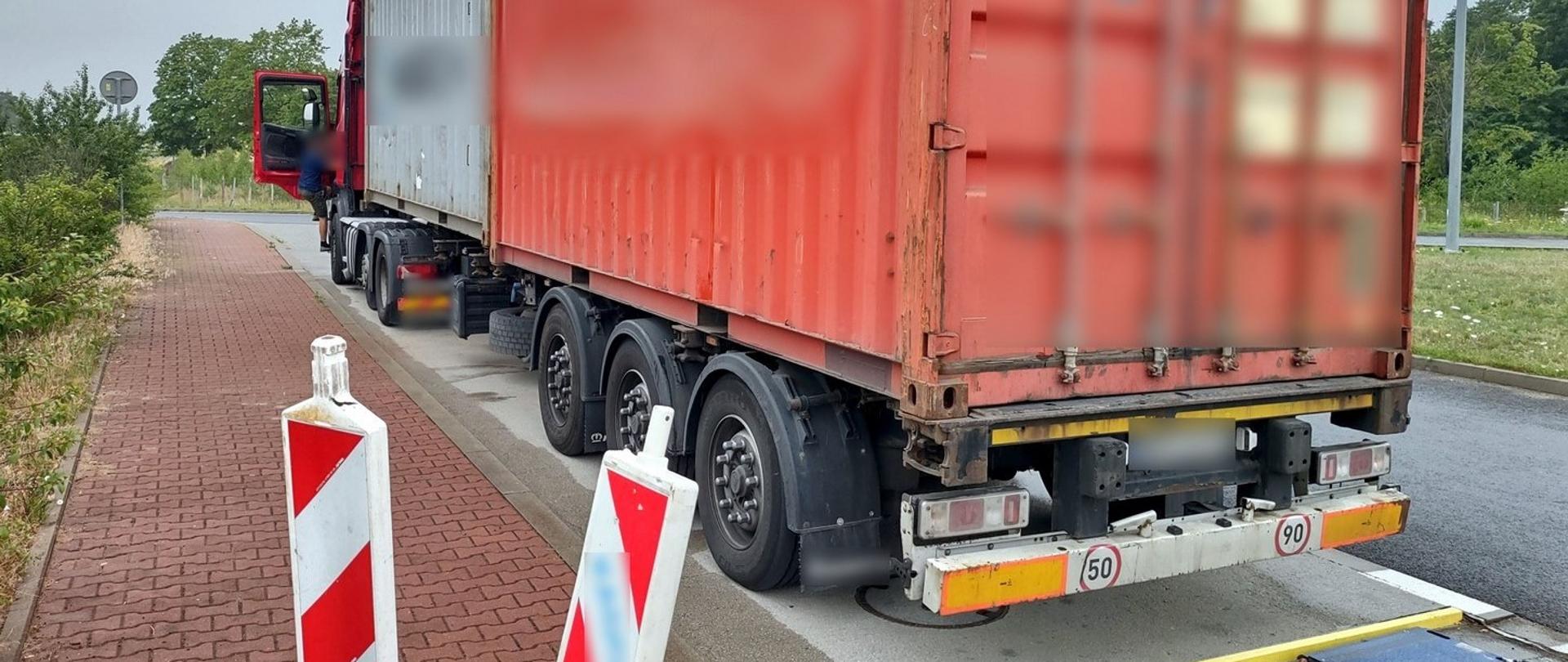 Ciągnik siodłowy z naczepą przewożącą dwa kontenery załadowane miodem gryczanym. Za naczepą są rozstawione wagi przenośne wielkopolskiej ITD.