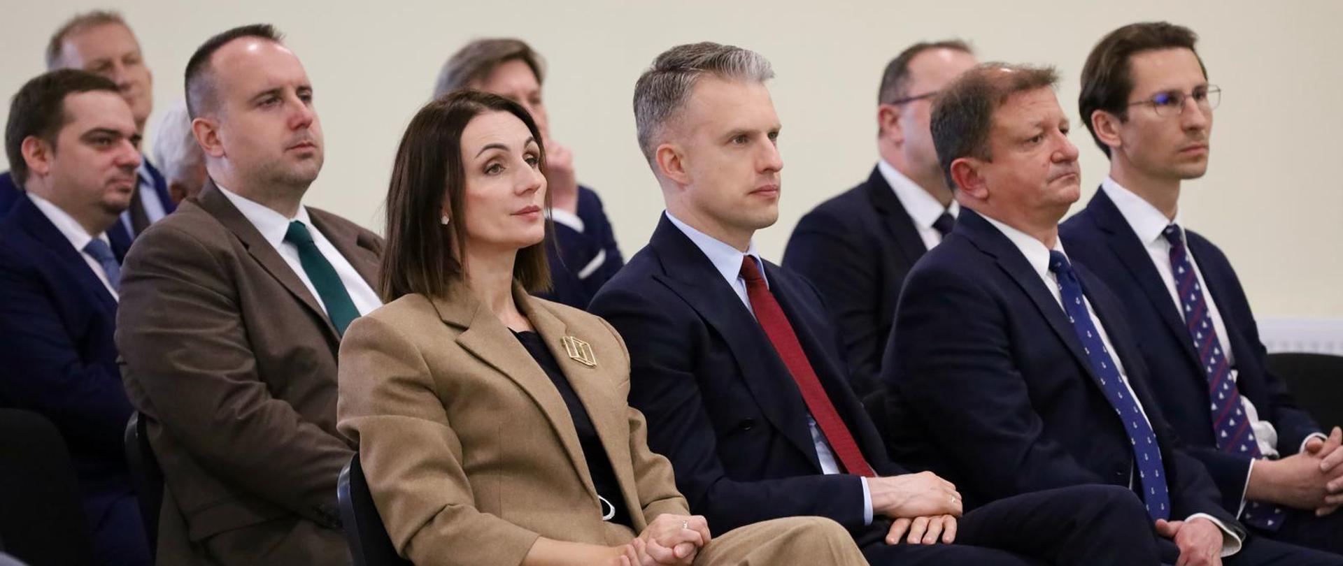 osoby siedza na krzesłach i przysłuchują się prezentowanym treściom