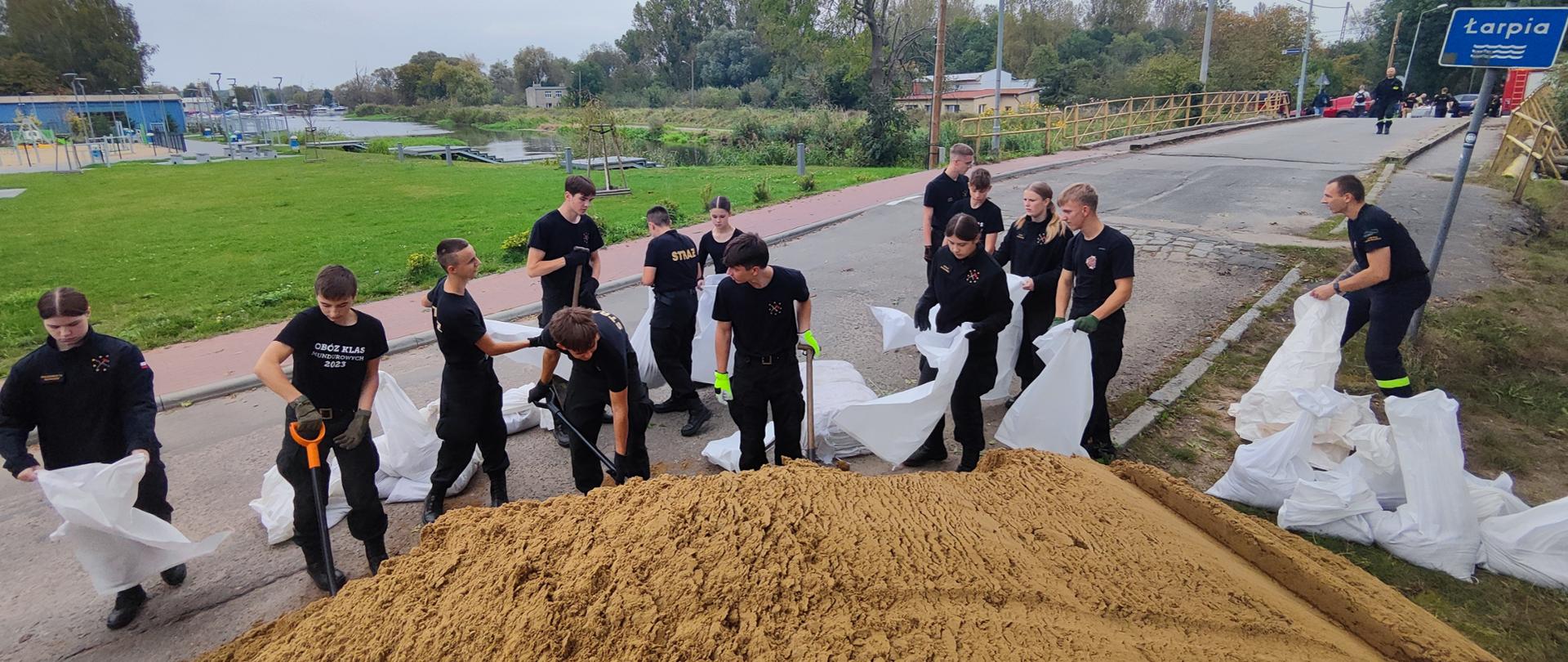 napełnianie worków piaskiem przez strażaków i uczniów klas pożarniczych