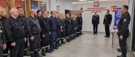 Na zdjęciu w sali konferencyjnej Komendy Powiatowej Państwowej Straży Pożarnej widoczni strażacy Państwowej Straży Pożarnej i druhowie kończący szkolenie ubrani w ubrania koszarowe w czarnym kolorze podczas uroczystego apelu kończącego szkolenie.