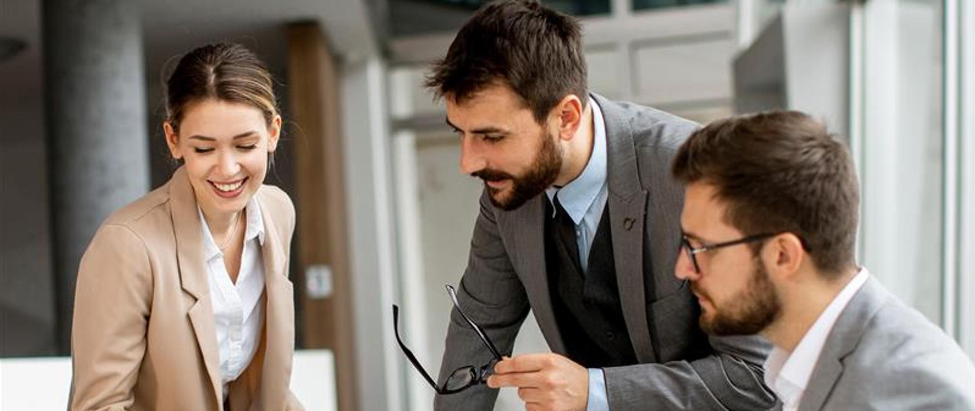 Kobieta i dwóch mężczyzn patrzą w komputer. 