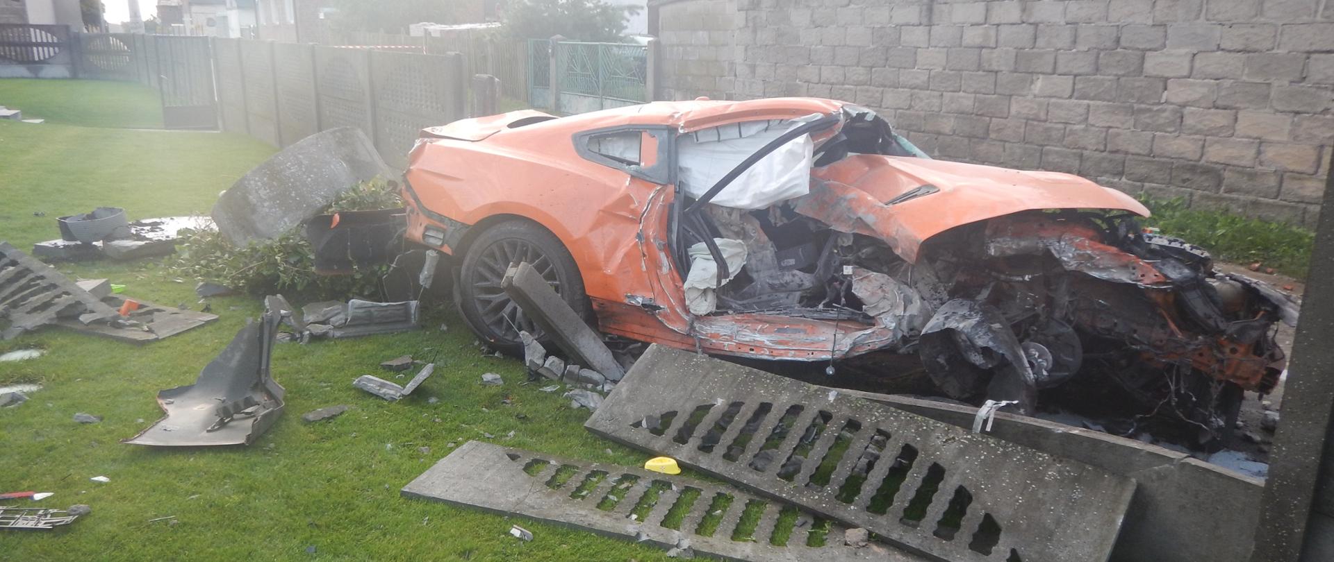 Zdjęcie przedstawia pomarańczowy samochód osobowy po wypadku drogowym.