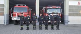 Minuta ciszy dla druhów z Jednostki OSP Żukowo - strażacy stoją przed strażnicą. W tle samochody pożarnicze.