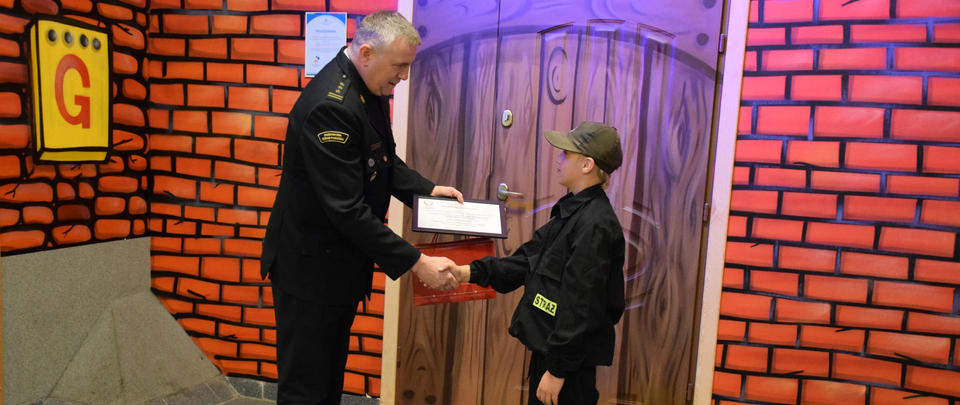 Zastępca Śląskiego Komendanta Wojewódzkiego PSP st. bryg. Rafał Świerczek wręcza nagrodę laureatowi Ogólnopolskiego Turnieju Wiedzy Pożarniczej „Młodzież Zapobiega Pożarom”