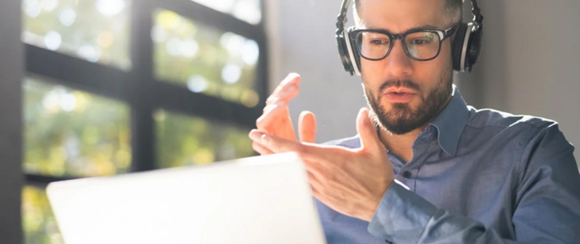 Osoba w słuchawkach przed laptopem, w jasnym pomieszczeniu z oknem i naturalnym światłem.