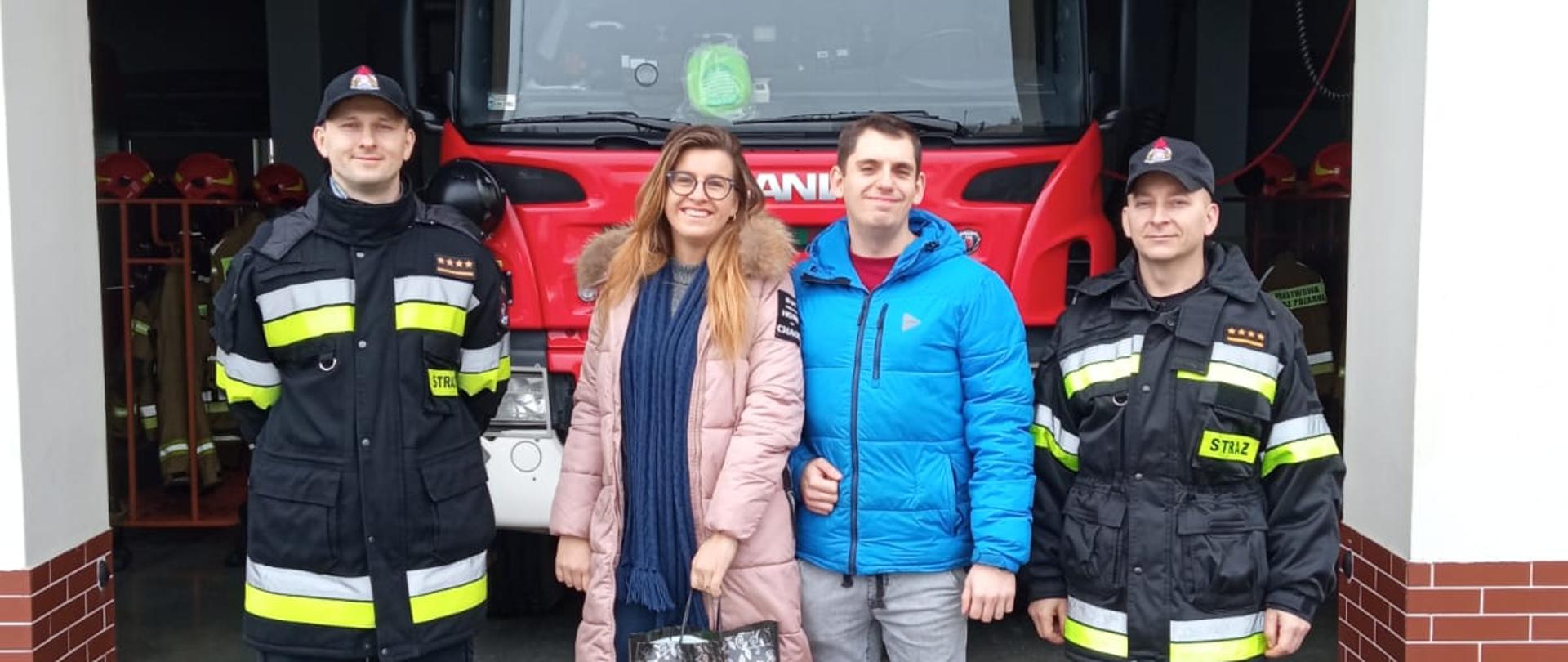 Zdjęcie przedstawia: Teren Komendy Powiatowej Państwowej Straży Pożarnej w Radziejowie na pierwszym planie karton z przekazywanymi Pluszakami, na drugim planie dowództwo jednostki ratowniczo-gaśniczej wraz z inicjatorami akcji zbieranie pluszaków dla dzieci uczestniczących w niebezpiecznych zdarzeniach.