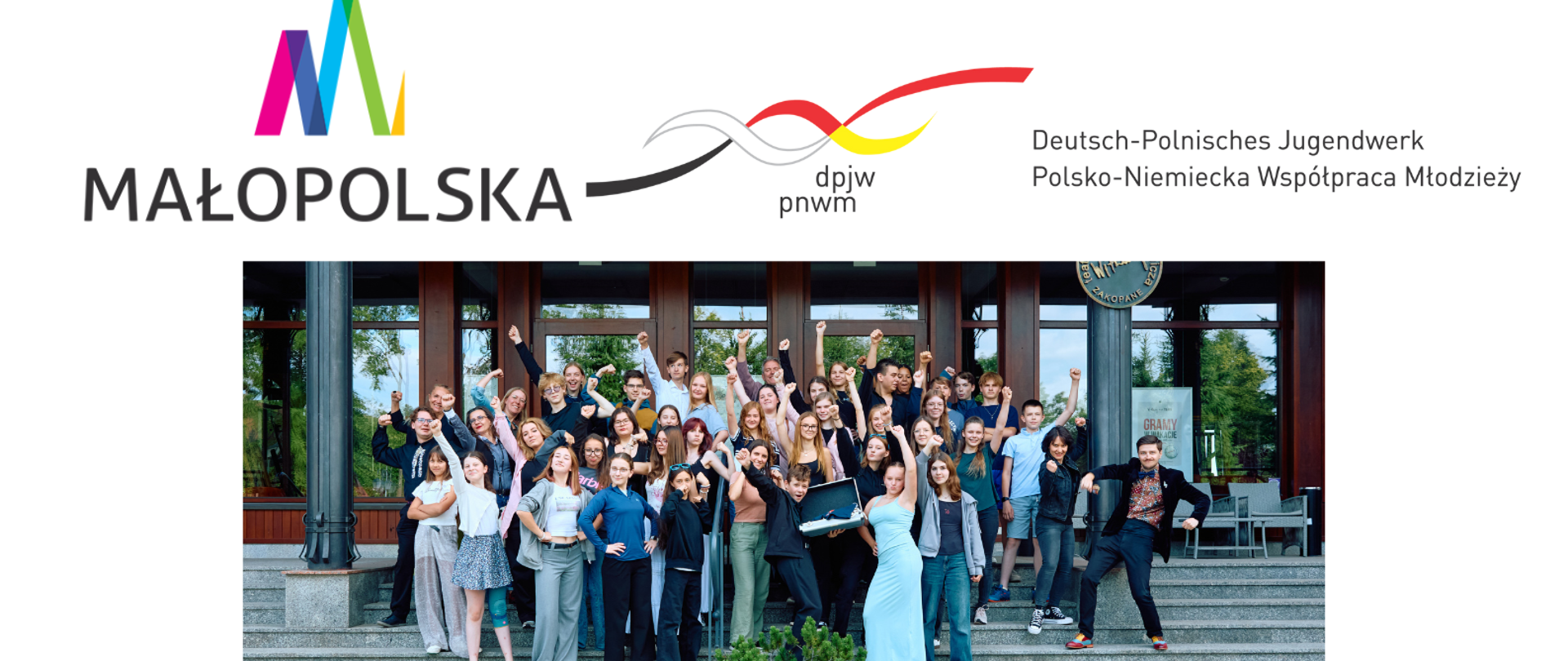Na zdjęciu w dolnej części grafiki znajduje się duża grupa młodych ludzi – około 50 osób – pozujących razem na schodach przed nowoczesnym budynkiem. Wszyscy są uśmiechnięci, niektórzy podnoszą ręce w górę lub przyjmują entuzjastyczne pozy, co tworzy radosną, energiczną atmosferę. Wśród nich są zarówno dziewczęta, jak i chłopcy w różnym wieku, najpewniej nastolatkowie lub młodzi dorośli.
Powyżej zdjęcia widnieją dwa logotypy: Po lewej stronie kolorowe logo z napisem „MAŁOPOLSKA”. Po prawej stronie logo z falującą linią w kolorach flag Polski i Niemiec oraz napisami: „dpjw pnwm” „Deutsch-Polnisches Jugendwerk / Polsko-Niemiecka Współpraca Młodzieży”. Grafika przedstawia uczestników wydarzenia programu wymiany młodzieżowej zorganizowanego w ramach polsko-niemieckiej współpracy, wspieranego przez województwo małopolskie.