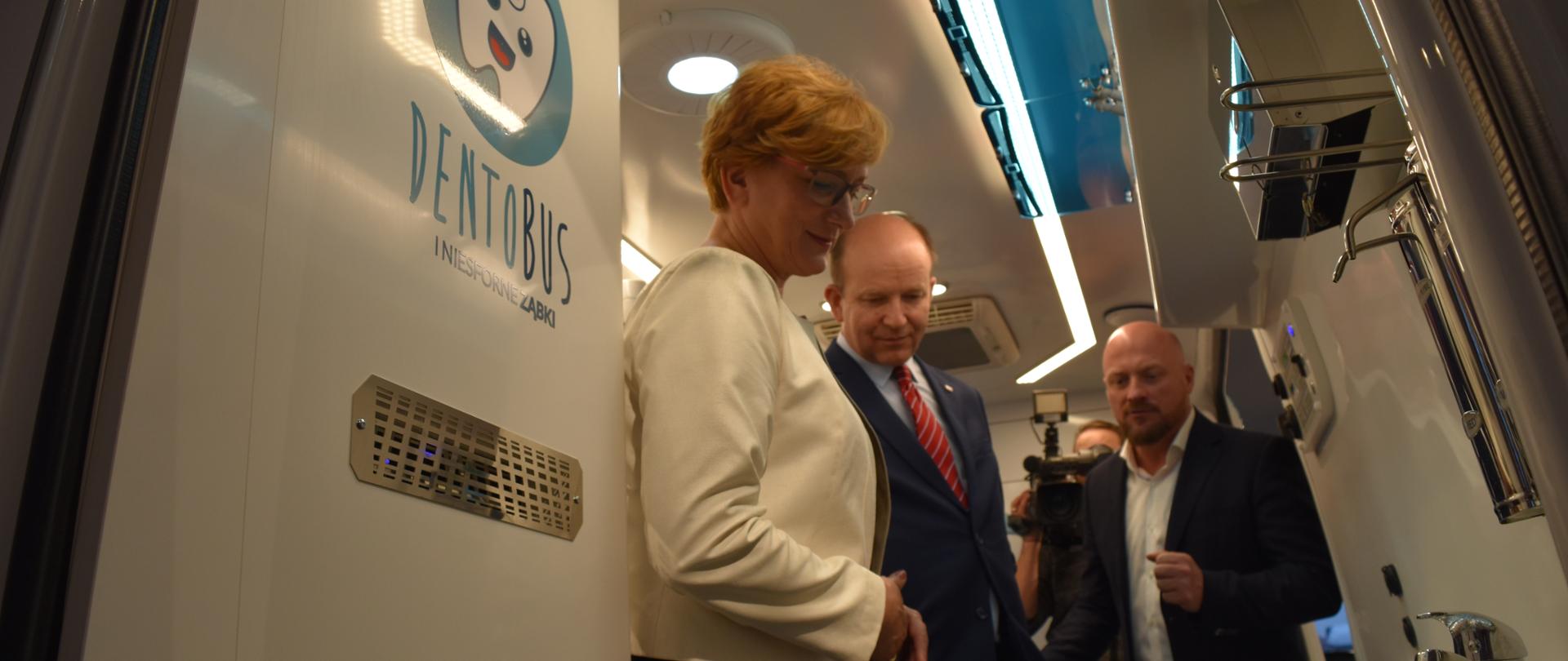 Przedstawiciel firmy, która wykonała dentobusy oprowadza ministra zdrowia Konstantego Radziwiłła oraz wiceminister Józefę Szczurek-Żelazko po wnętrzu pojazdu. W tle widać operatora kamery.