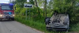 Zdjęcie przedstawia przewrócony samochód na dach w rowie.