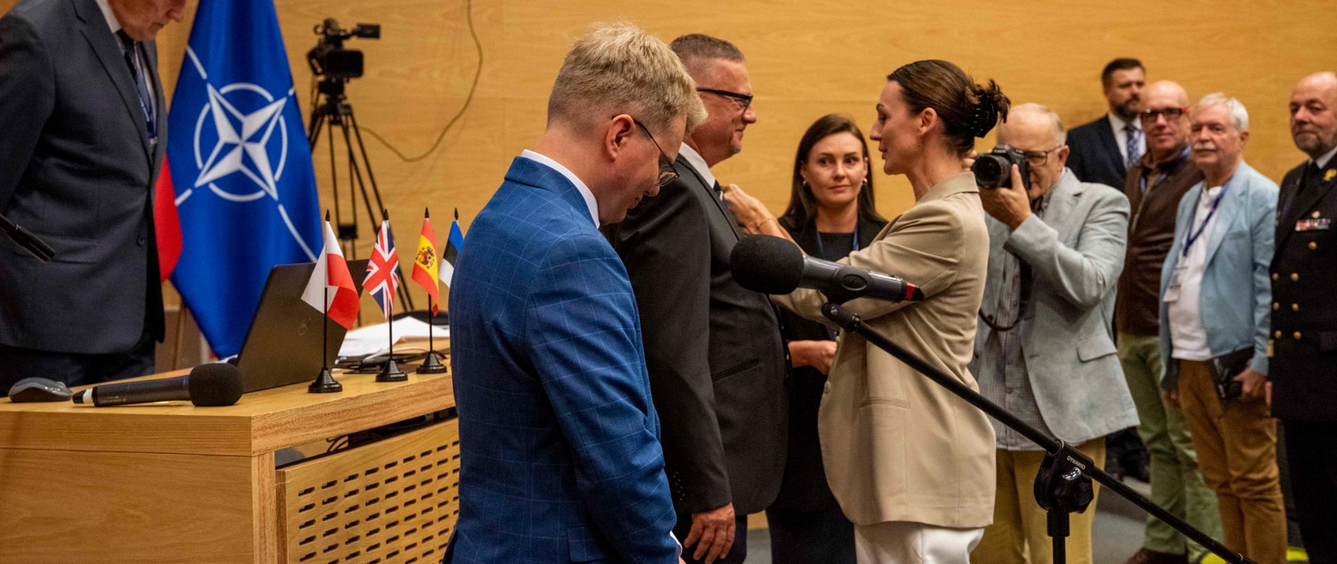 kobieta (wojewoda) przypina medal mężczyźnie, wokół kilka osób w tym w mundurach marynarki wojennej