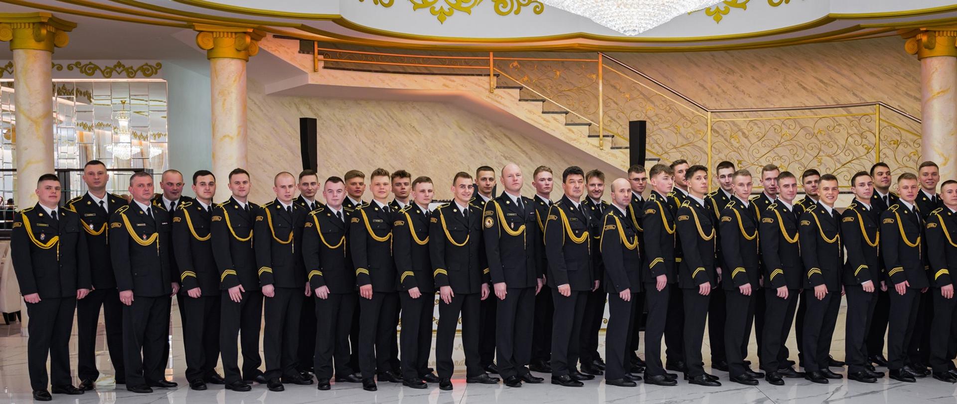 Grupowe zdjęcie plutonu 1 DSA CS PSP, w towarzystwie Komendanta CS PSP oraz Zastępcy Komendanta CS PSP podczas "Balu kadeta". Wszyscy w mundurach galowych
