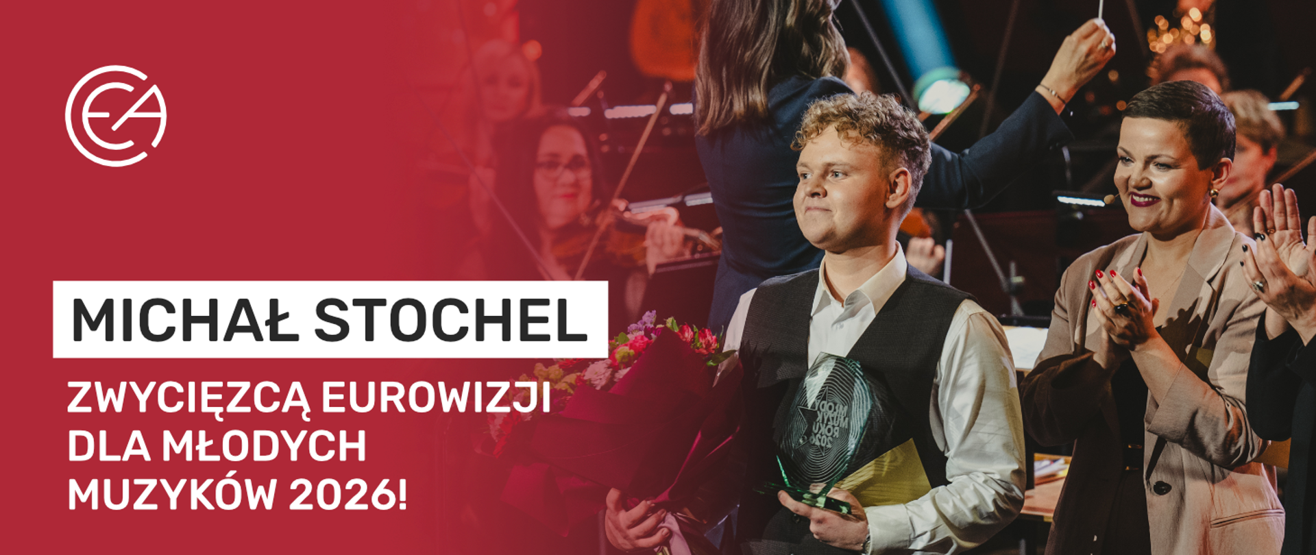 Baner gratulacyjny z białym logo CEA na czerwonym tle po lewej stronie oraz dużym napisem: „MICHAŁ STOCHEL ZWYCIĘZCĄ EUROWIZJI DLA MŁODYCH MUZYKÓW 2026!”. Po prawej stronie znajduje się zdjęcie uśmiechniętego młodego mężczyzny trzymającego szklaną statuetkę oraz bukiet kwiatów, obok którego klaszcze kobieta. W tle widoczna jest rozmyta scena z koncertu z udziałem orkiestry.