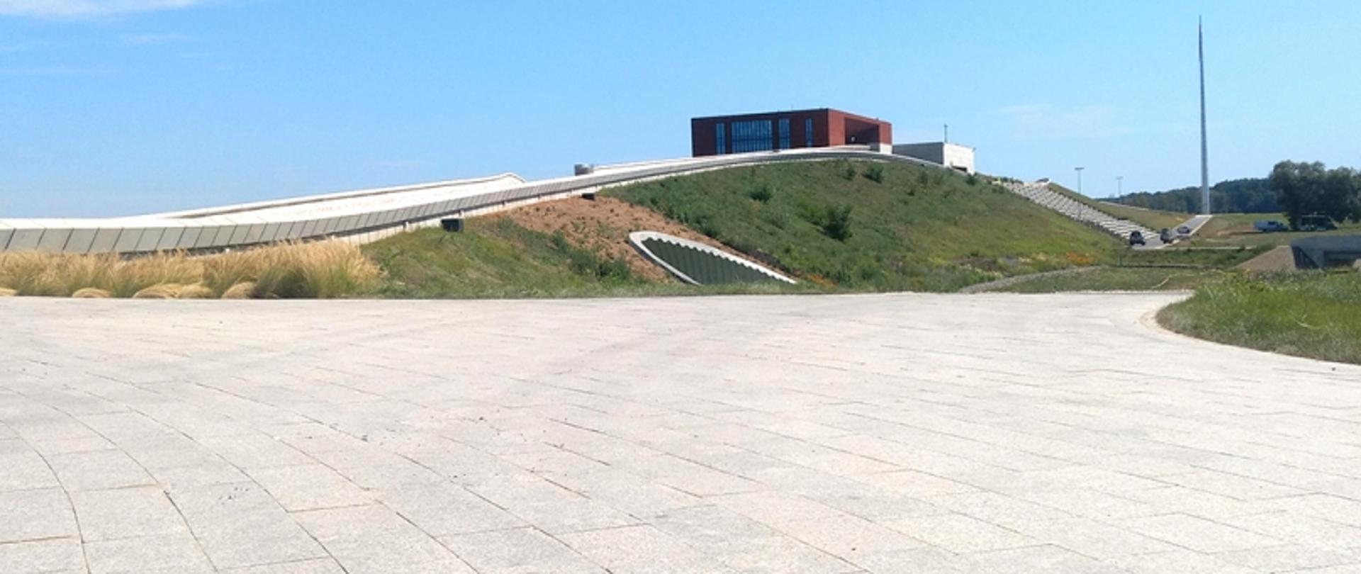 Nowoczesna konstrukcja z pochylonymi dachami na wzgórzu, z utwardzoną drogą prowadzącą do wejścia.