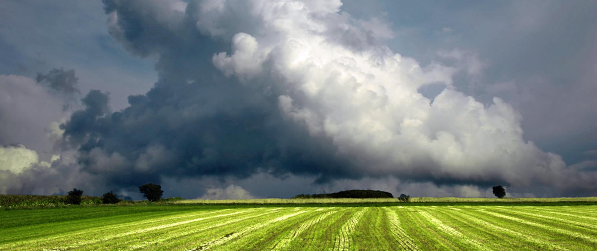 Złowrogie chmury burzowe Cumulonimbus piętrzące się nad zielonymi łąkami