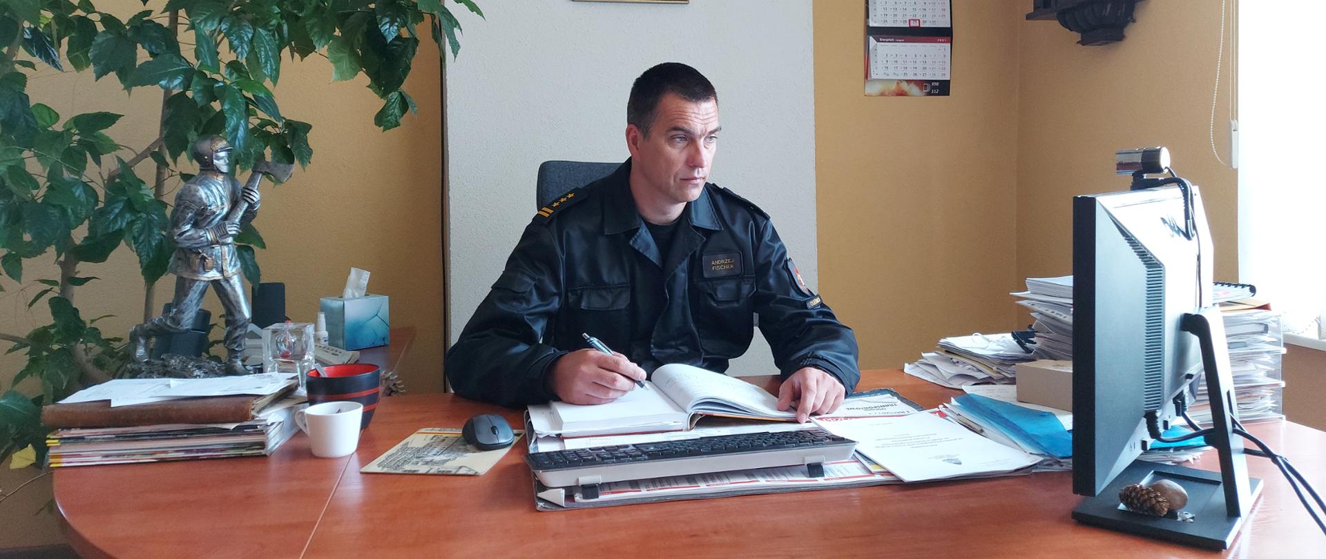 Na zdjęciu widać Komendanta Powiatowego PSP w Oleśnicy przed monitorem komputera. W tle Godło Rzeczypospolitej Polskiej. 