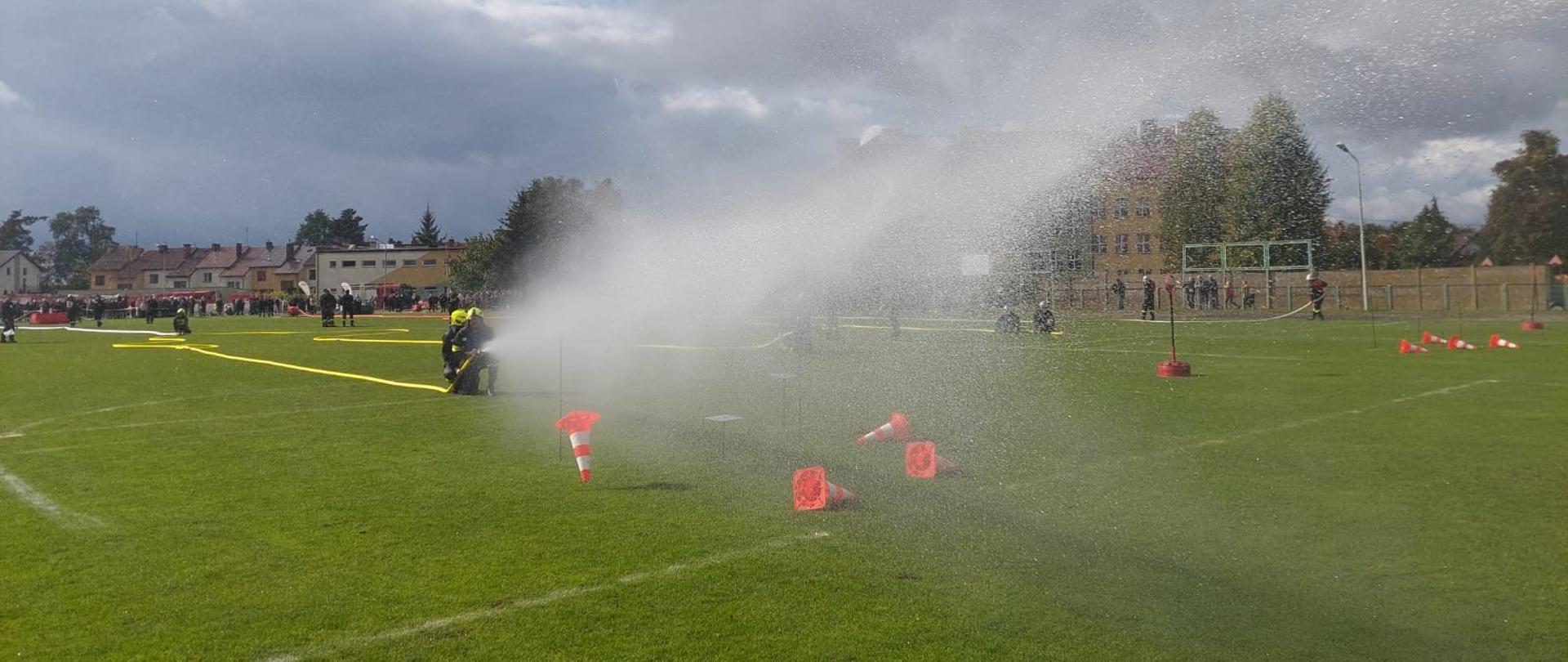 Zawodnicy OSP w trakcie wykonywania konkurencji ćwiczenie bojowe. Strącili pachołki ze stojaków przy pomocy prądów wody.